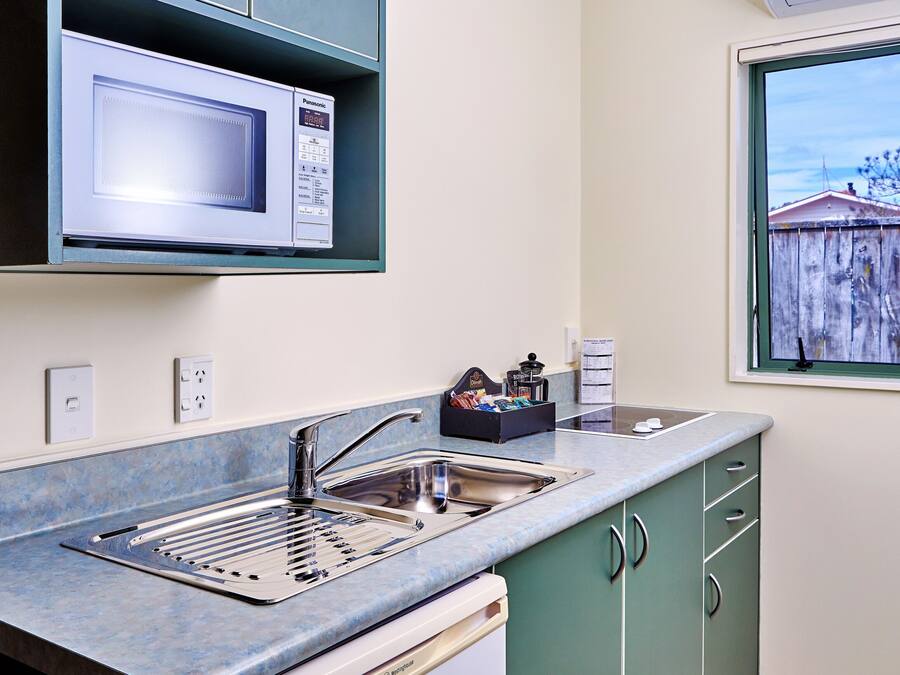 A compact kitchen with a built-in microwave, stainless steel sink, and a window with a view of a wooden fence.