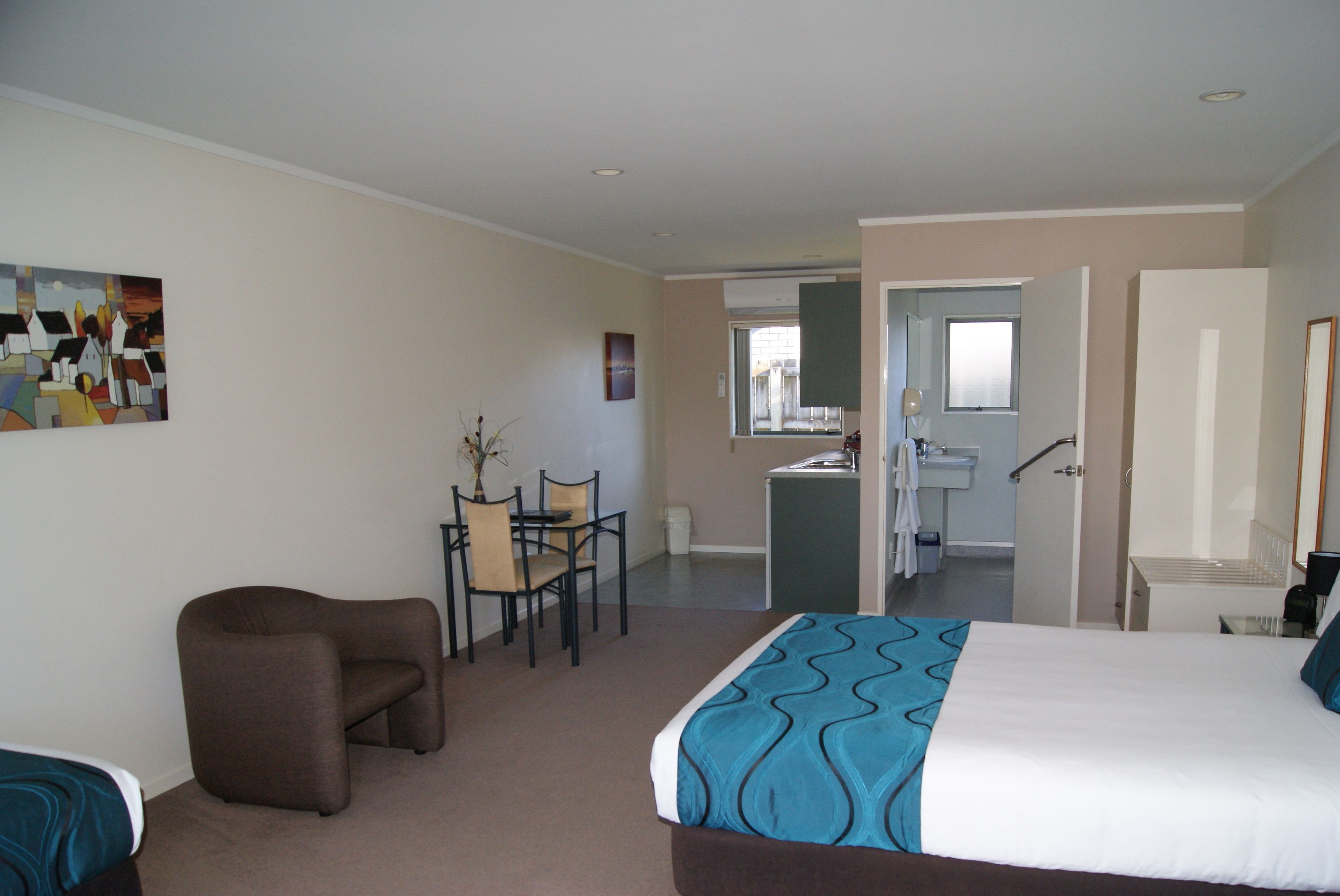 A hotel room with a bed, a desk, a chair, and a kitchenette.