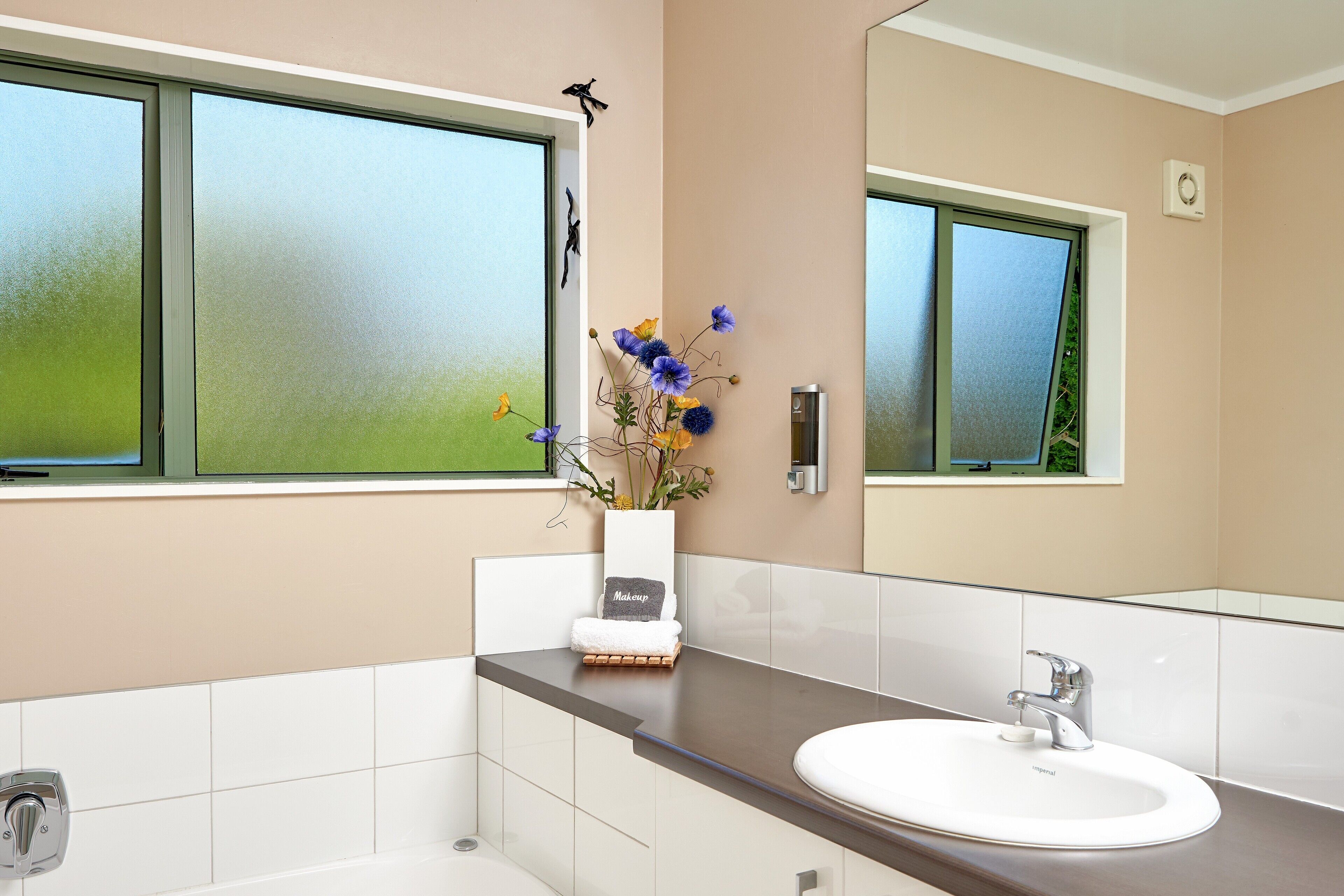 A modern bathroom with a large window, a white sink, and a vase with flowers on the counter.