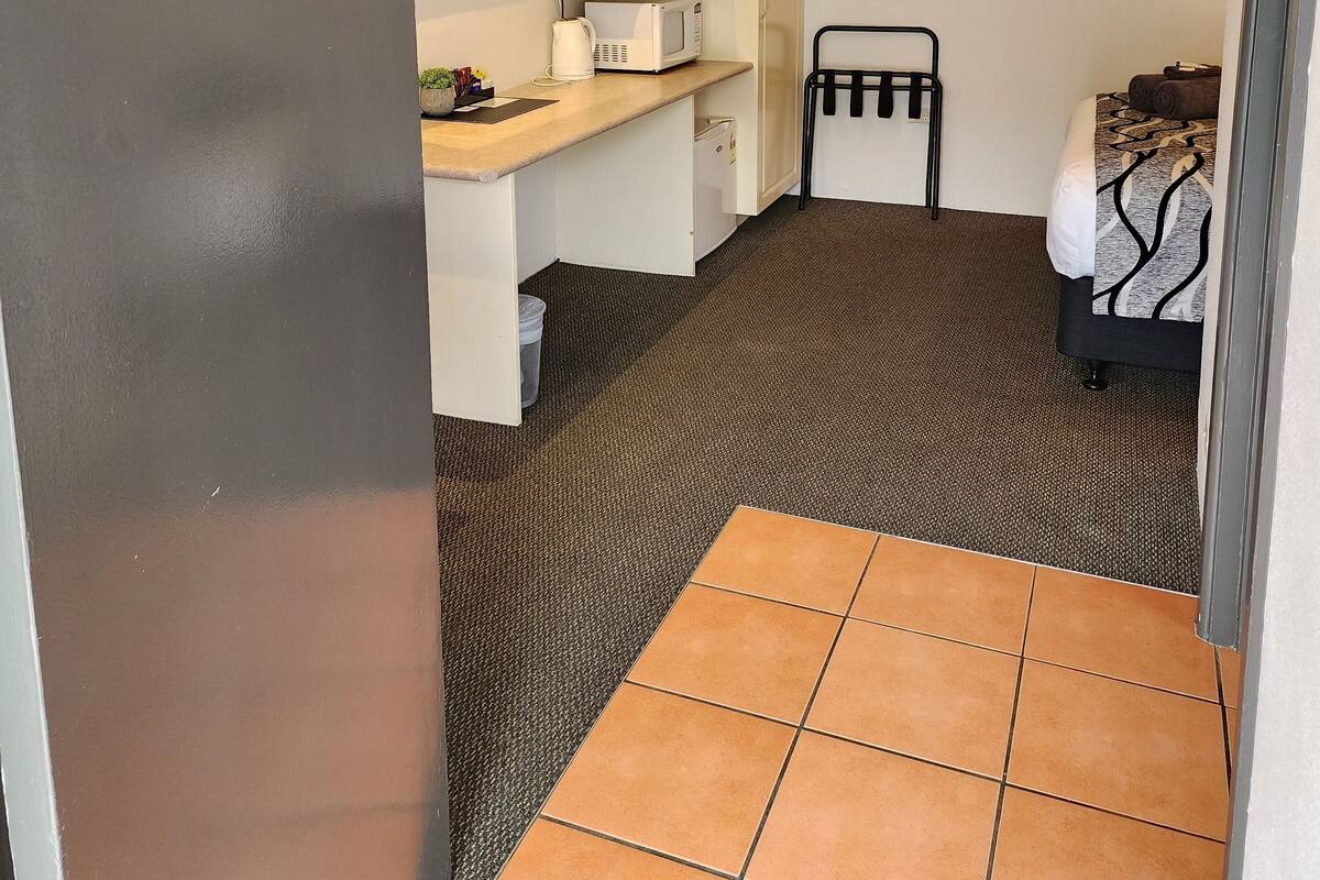 A compact hotel room with a bed, a desk with a flat-screen TV, a microwave, a coffee maker, and a ceiling fan.