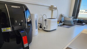 Una cocina con cafetera, tostadora y una pila de platos sobre la encimera.