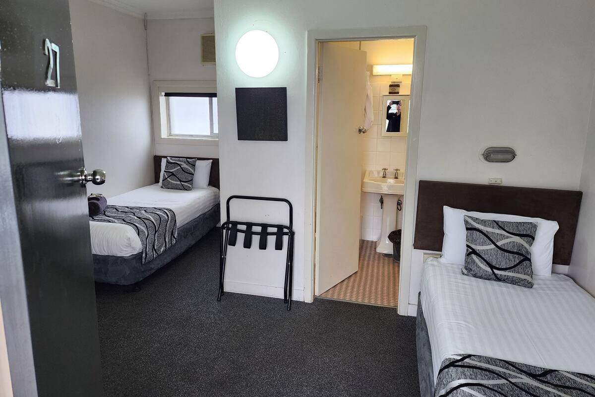 A hotel room with two beds, a small seating area, a bathroom with a sink and mirror, and a ceiling fan.