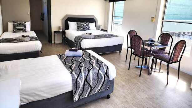 Habitación de hotel con dos camas, zona de comedor y balcón con vistas.