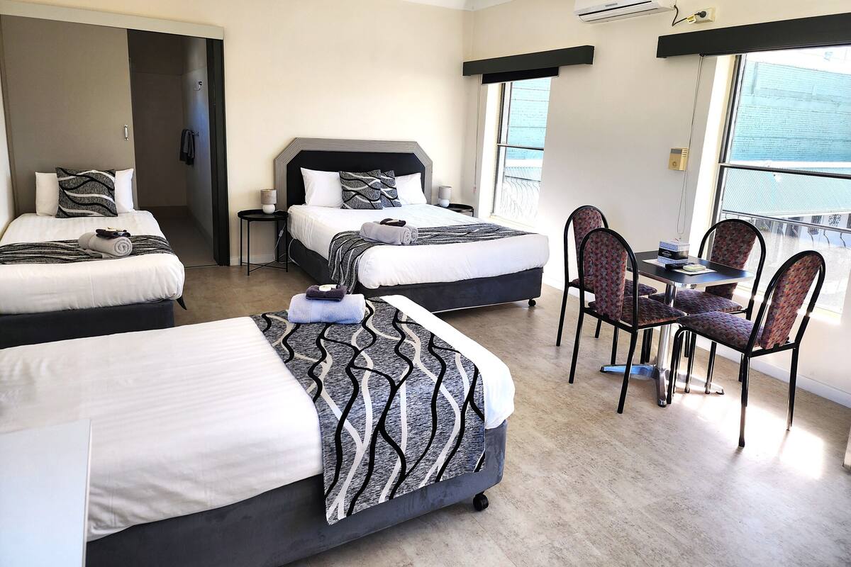 A hotel room with two beds, a dining area, and a balcony with a view.