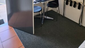 Una habitación pequeña con un escritorio, dos sillas, un televisor montado en la pared y un perchero.