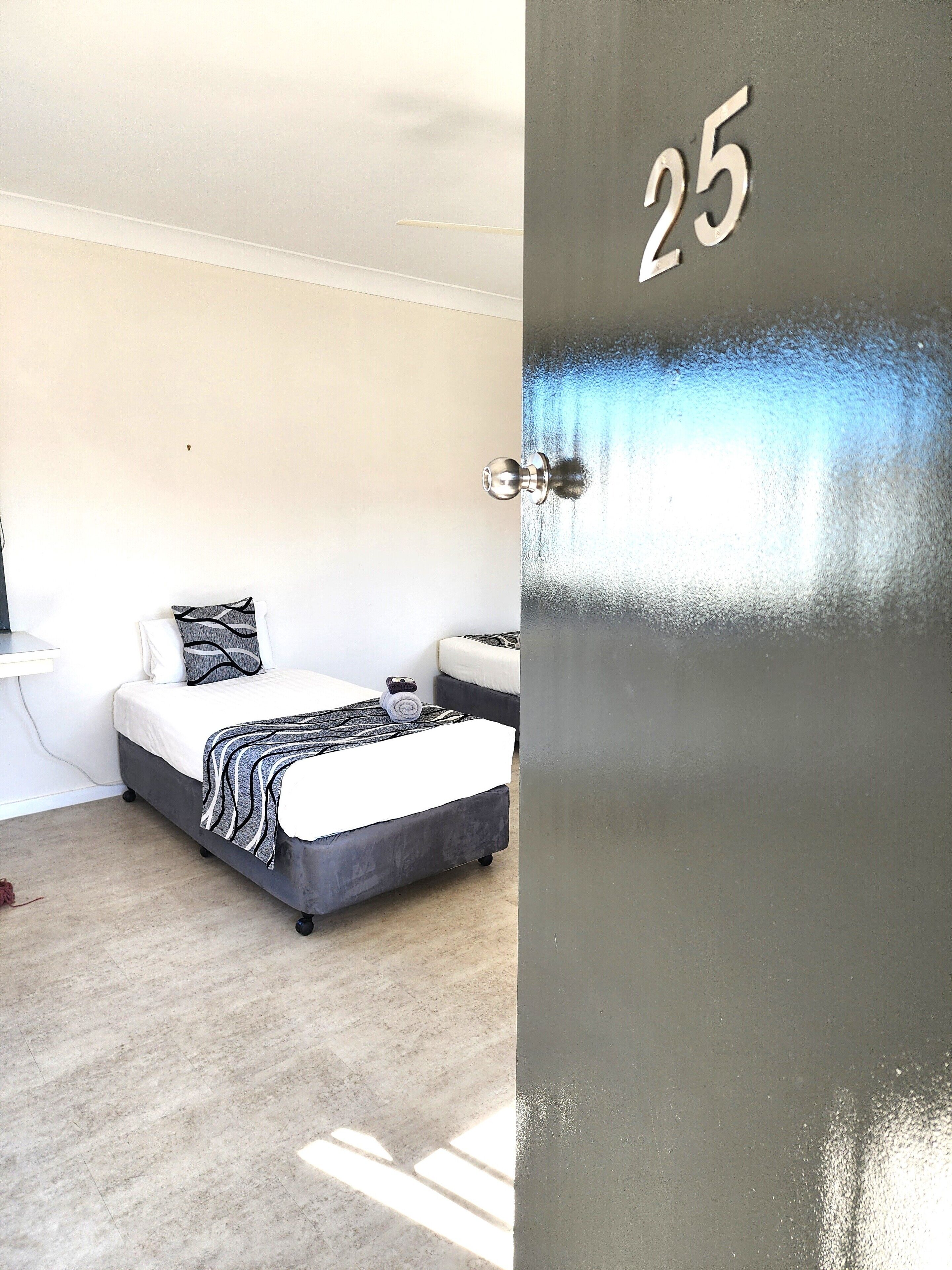 A bedroom with a bed, a bedside table, and a door with the number 25.