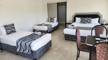 A hotel room with three beds, a desk, and a chair.