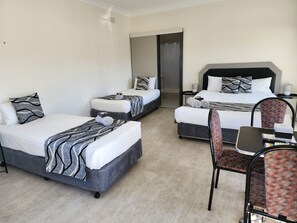 A hotel room with three beds, a desk, and a chair.