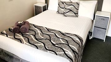 A neatly made bed with a patterned bedspread, two pillows, and a decorative item on the bed. There are two bedside tables with lamps and a small drawer unit beside the bed.