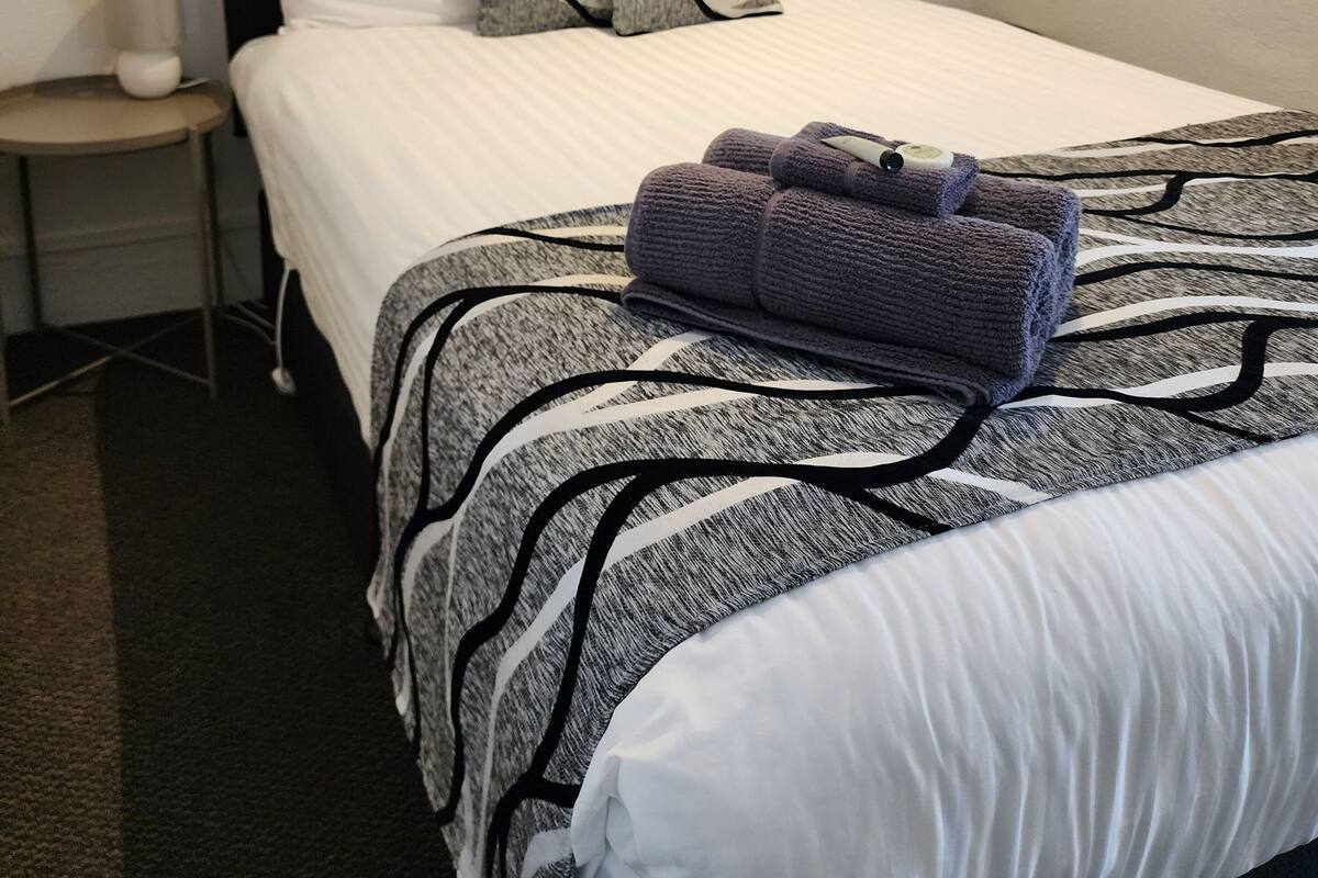 A neatly made bed with white and gray striped bedding, two pillows with a black and gray pattern, and a folded towel on the bed.