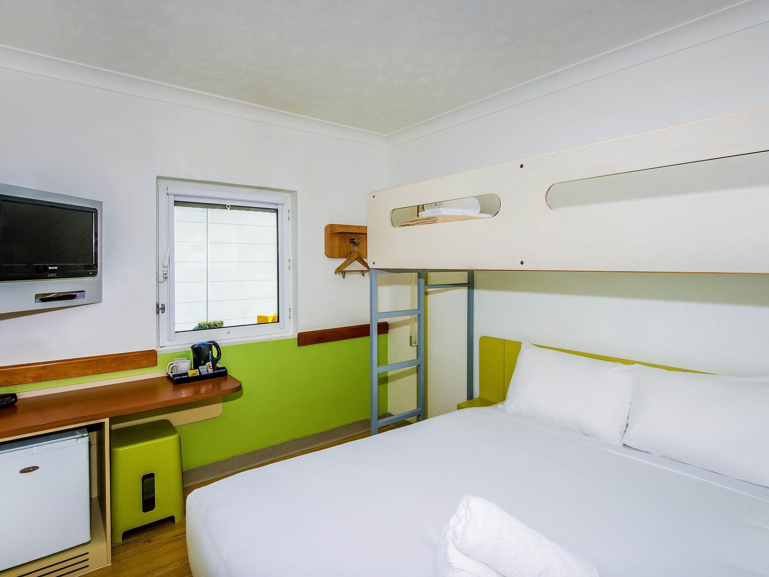 Habitación de hotel con literas, un televisor, un escritorio pequeño con cafetera y una ventana.