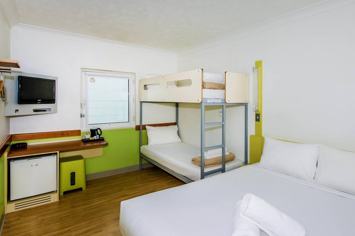 Une chambre d’hôtel avec des lits superposés, un bureau avec une télévision, un petit réfrigérateur et une fenêtre.