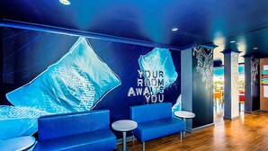A modern hotel lobby with blue seating, a large wall mural, and a wooden floor.