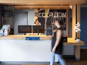 Ein Empfangstresen mit Schilder zur Angabe der Öffnungszeiten, einem Computer und Informationsbroschüren.