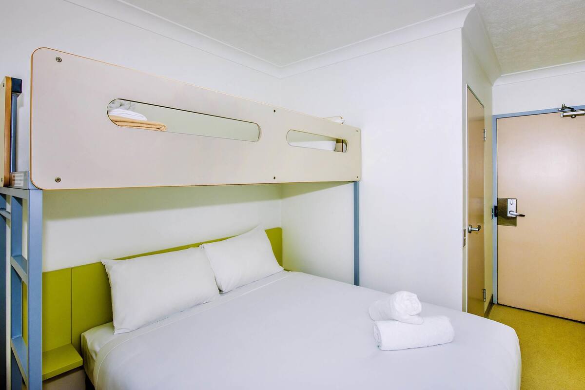 Un lit superposé avec une tête de lit, un lit simple avec des oreillers et une porte sur la droite.