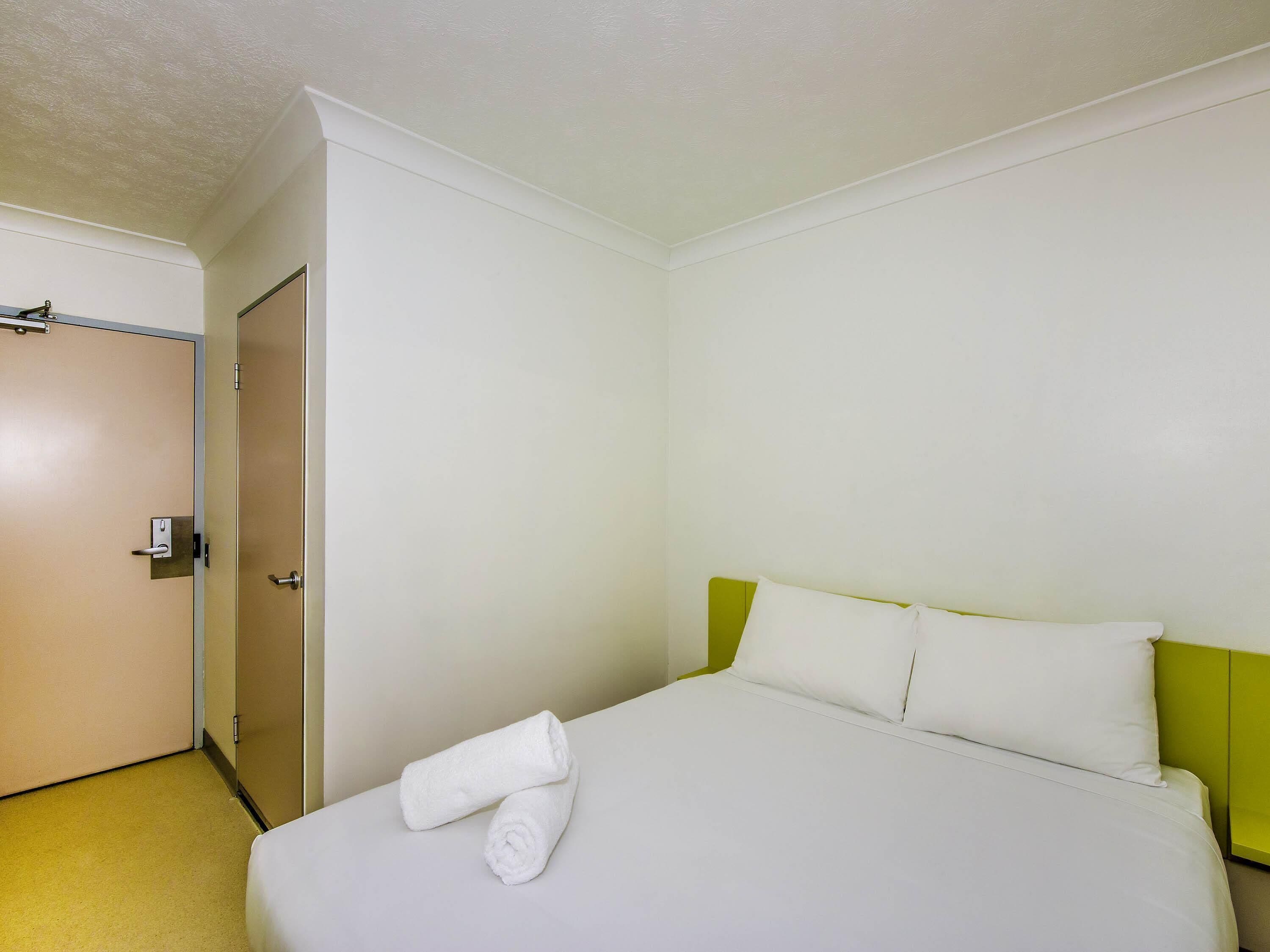A hotel room with a bed, a door, and a green headboard.