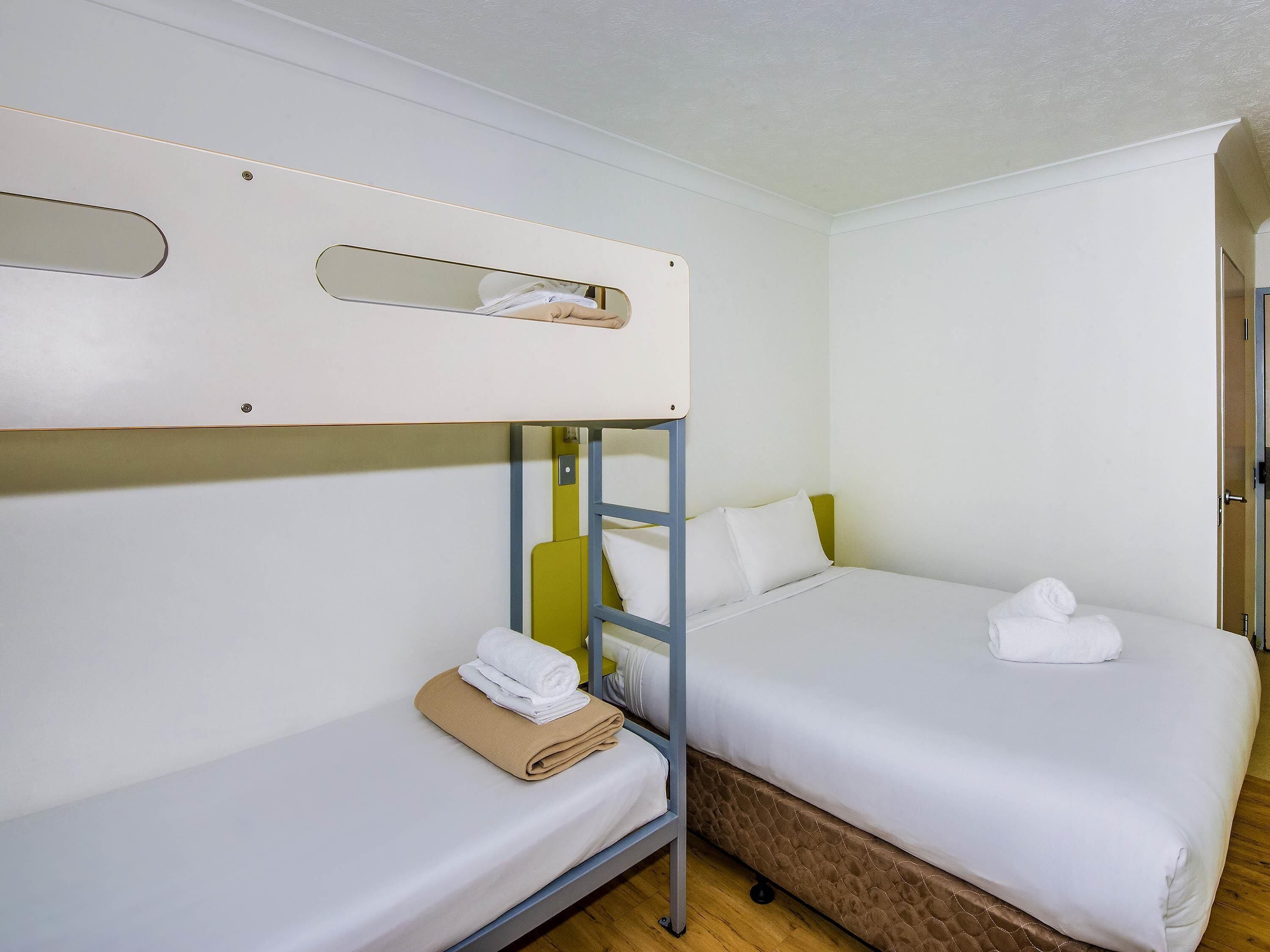 Habitación con una cama individual y una litera, ambas con ropa de cama blanca y una toalla sobre la cama individual.