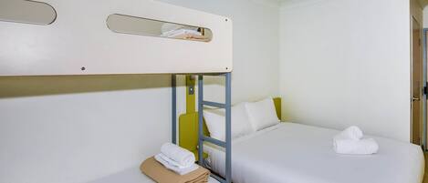 Habitación con una cama individual y una litera, ambas con ropa de cama blanca y una toalla sobre la cama individual.