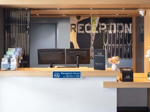 Mostrador de recepción con un cartel que indica el horario, una computadora, un atril con mapas y una pared con una exhibición de joyería.