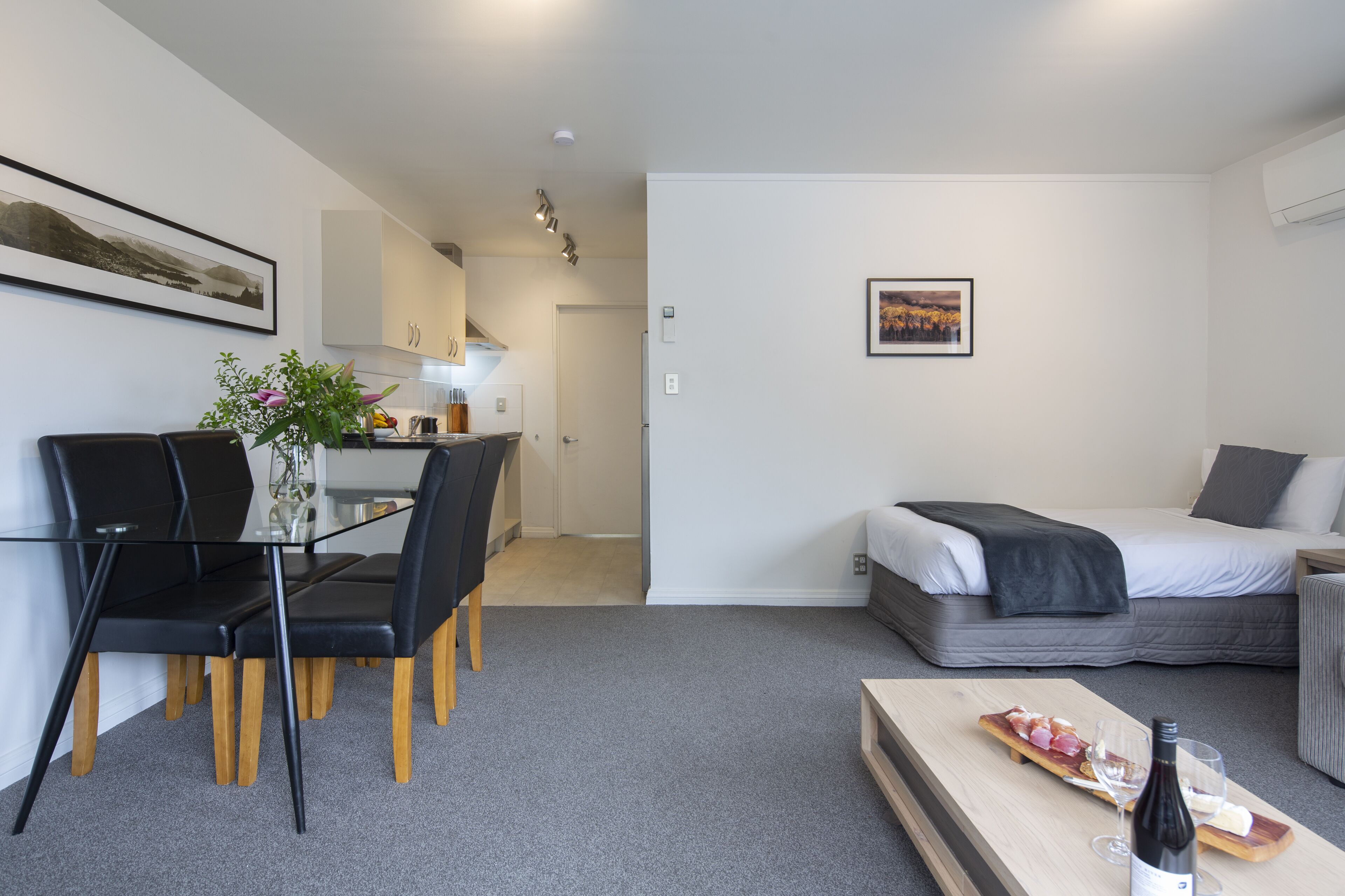 A modern, compact living space with a dining area, kitchenette, and a bed.
