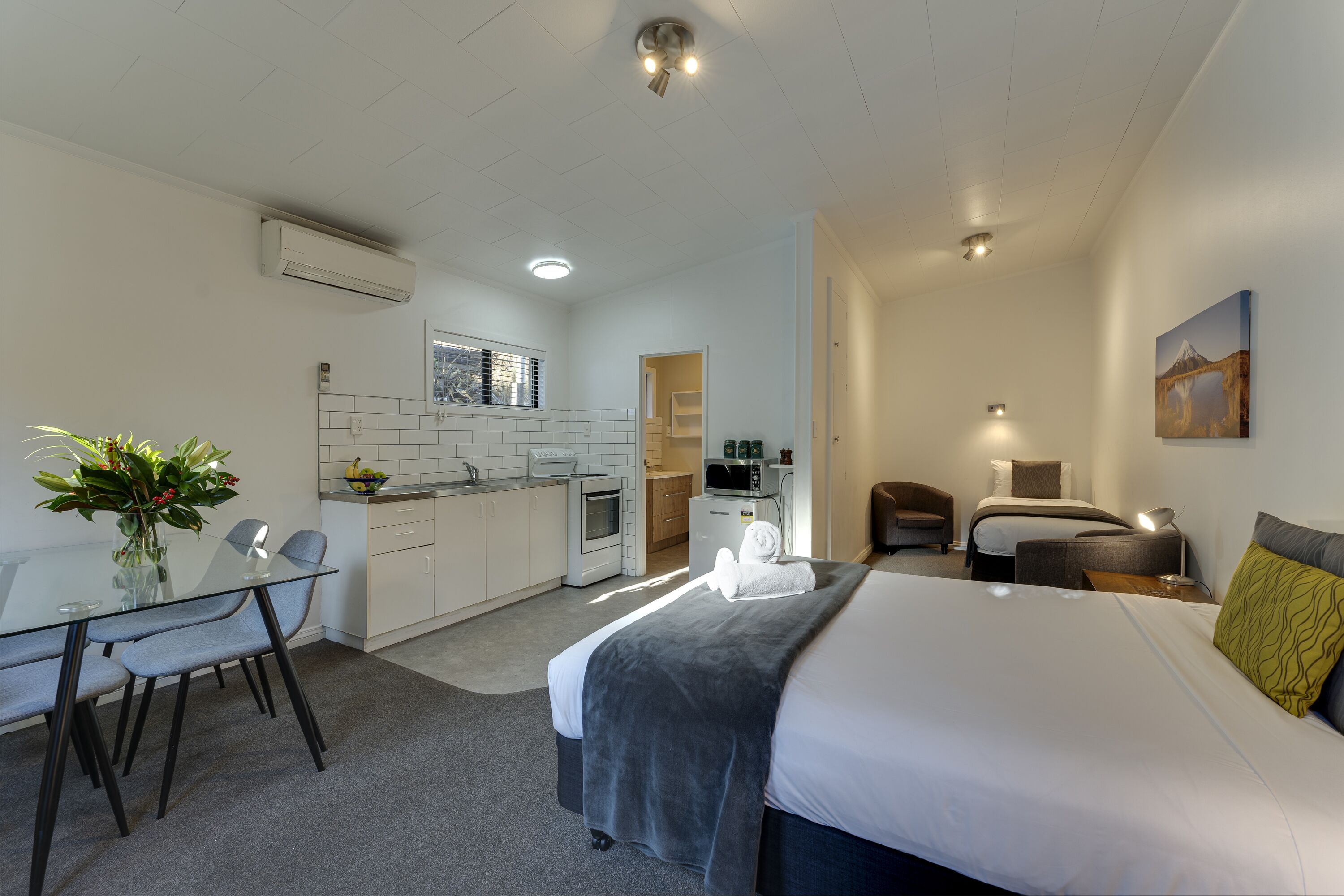 Een moderne hotelkamer met een groot bed, een bureau met stoelen, een kitchenette en een badkamer.