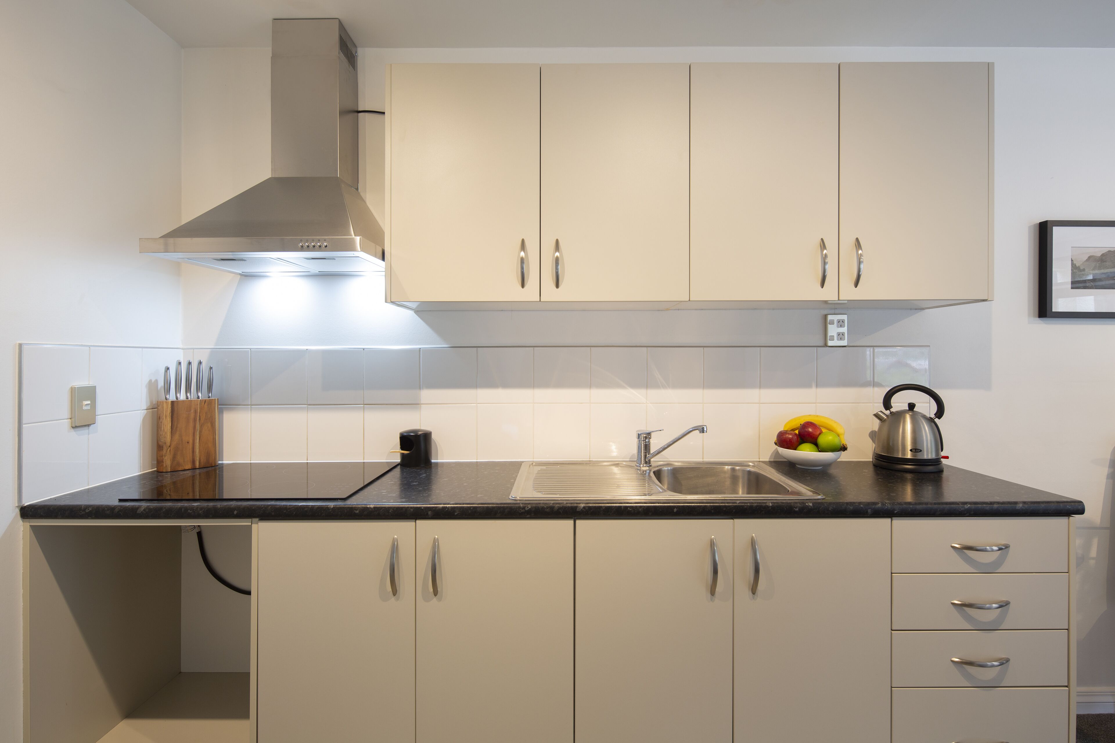 A modern kitchen with a stainless steel range hood, a double sink, and a fruit bowl on the countertop.