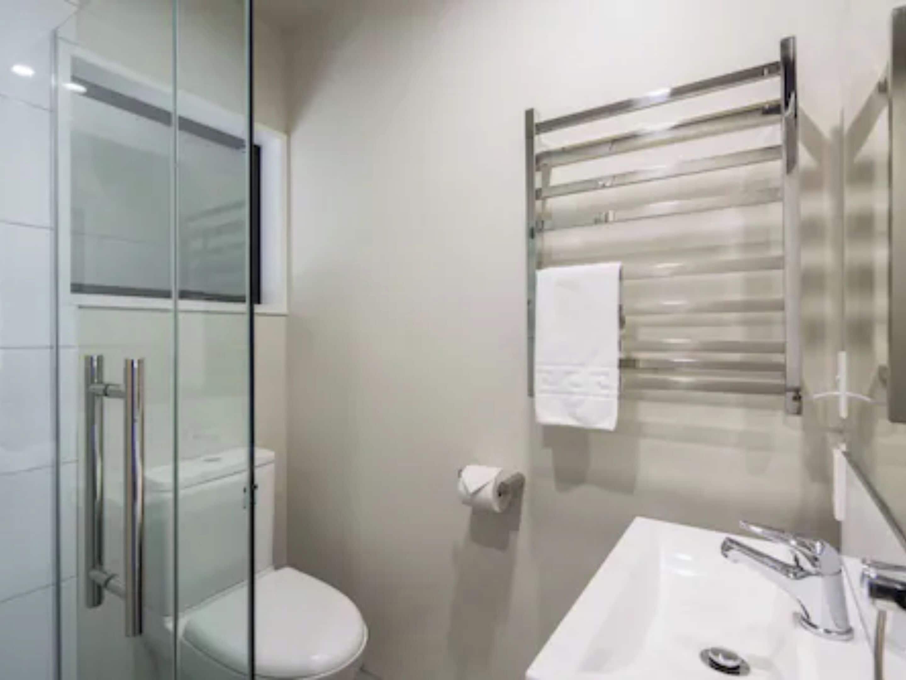 A modern bathroom with a glass shower enclosure, a white toilet, a sink with a chrome faucet, and a towel rack with a white towel.