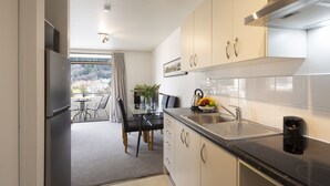 A modern kitchen with a refrigerator, sink, and dining area with chairs and a table. - Abba Court Motel & Apartments (Queenstown)