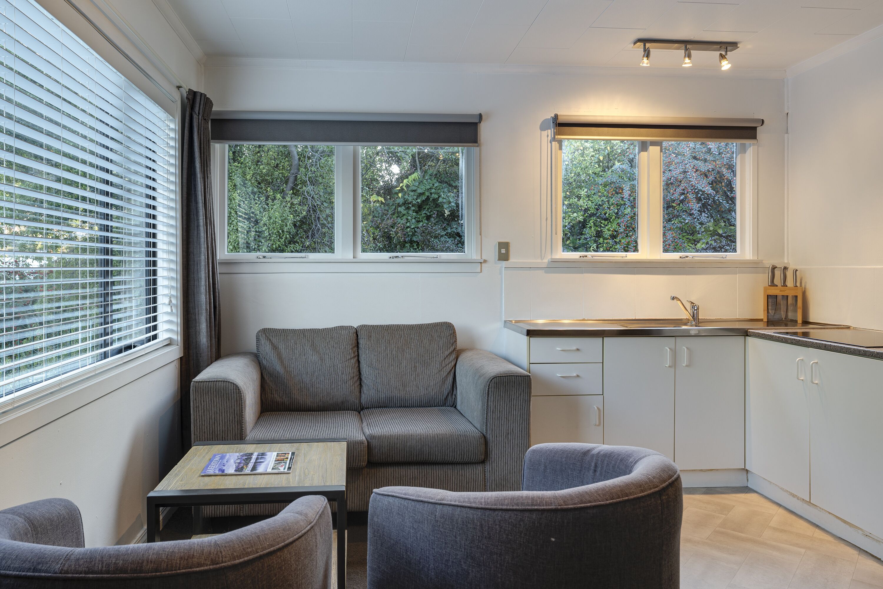 Une cuisine compacte avec un canapé et deux fauteuils, une petite table et une fenêtre avec des stores.