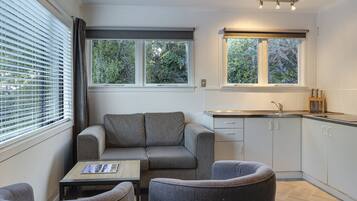 A compact kitchen with a sofa and two armchairs, a small table, and a window with blinds.