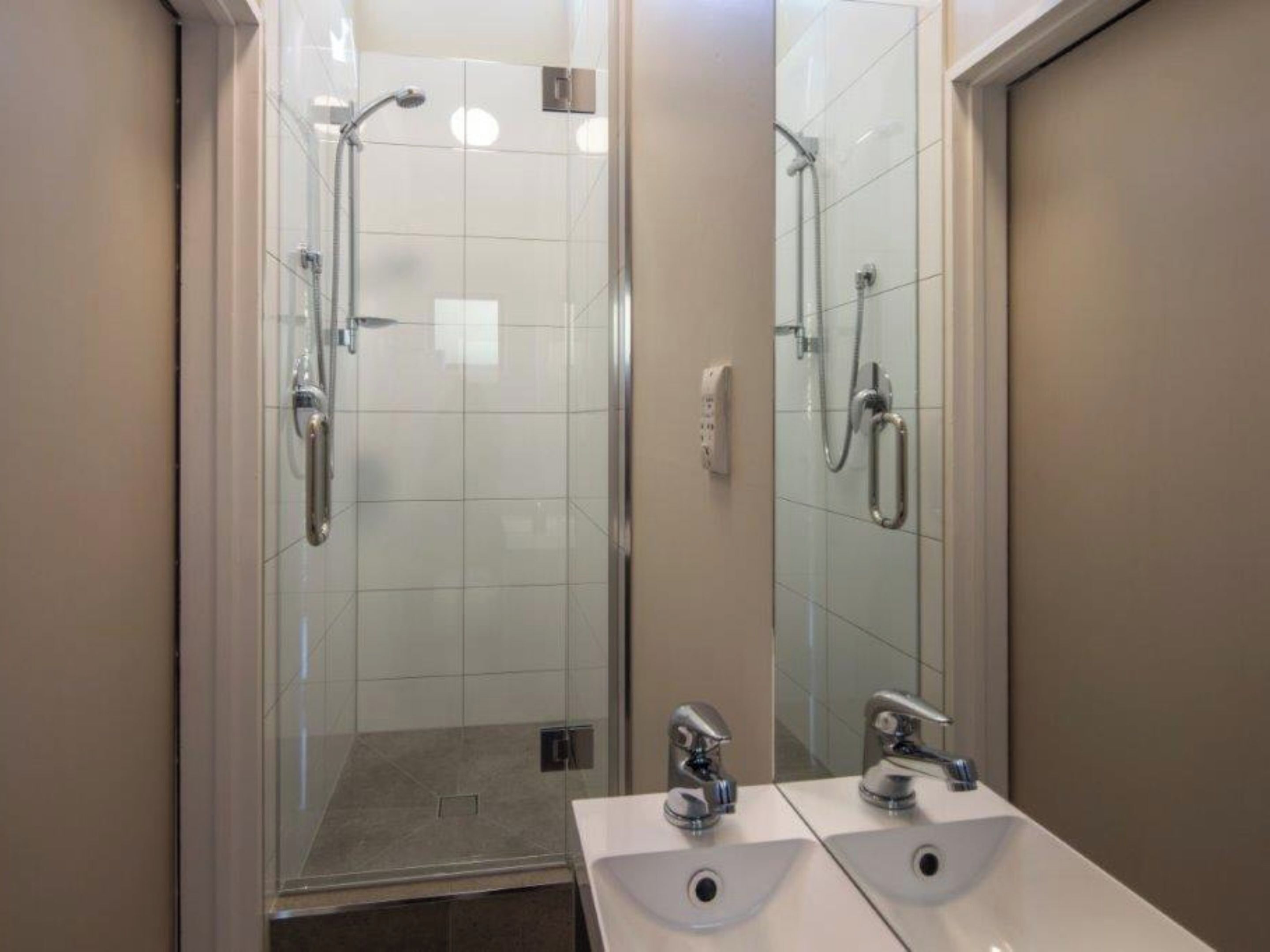 A modern bathroom with a glass-enclosed shower, two sinks, and a mirror.