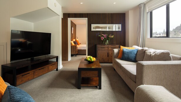 A modern living room with a flat-screen TV, a wooden coffee table, a sofa, and a cabinet. - Abba Court Motel & Apartments (Queenstown)