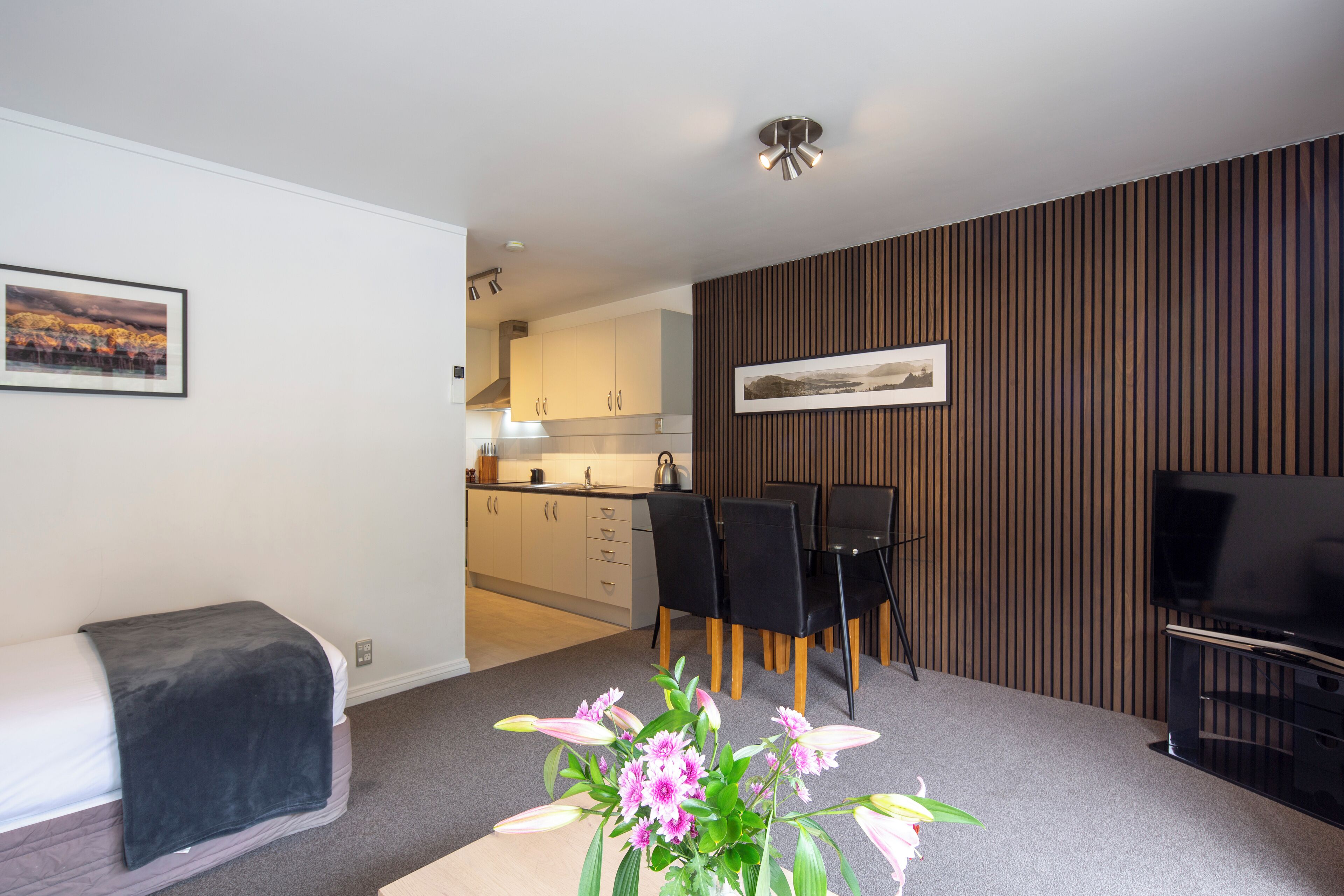 A modern living room with a sofa, a dining table with chairs, a TV, and a kitchen in the background.