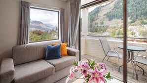 A modern hotel room with a sofa, a small table with flowers, and a balcony with a view of the mountains. - Abba Court Motel & Apartments (Queenstown)