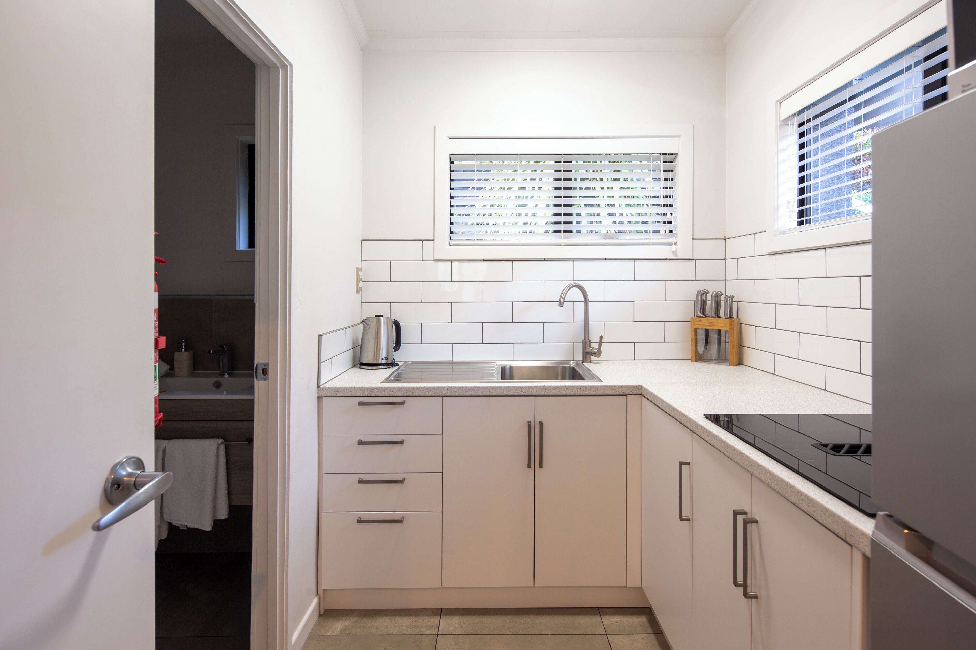 A compact kitchen with a sink, stove, and window with blinds.