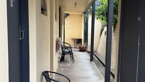Un pasillo techado con suelo de hormigón, una fila de sillas y una puerta con el número 4.