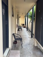 Un pasillo techado con suelo de hormigón, una fila de sillas y una puerta con el número 4.