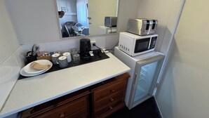 Una kitchenette compacta con microondas, cafetera y un refrigerador pequeño.