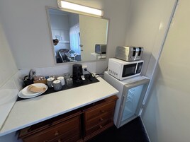 Una kitchenette compacta con microondas, cafetera y un refrigerador pequeño.