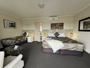 Habitación de hotel con una cama grande, una cama más pequeña, un rincón de estar con una silla, una mesita y un espejo.