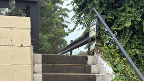 Un conjunto de escalones de concreto con líneas amarillas de seguridad, un letrero de precaución y una barandilla metálica.
