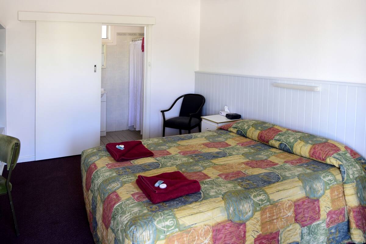 A hotel room with a bed, a chair, a desk, and a bathroom visible through an open door.