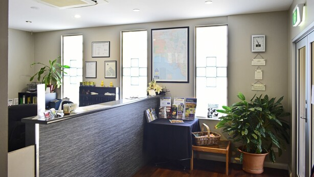 A reception area with a reception desk, framed maps, a clock, and a potted plant.