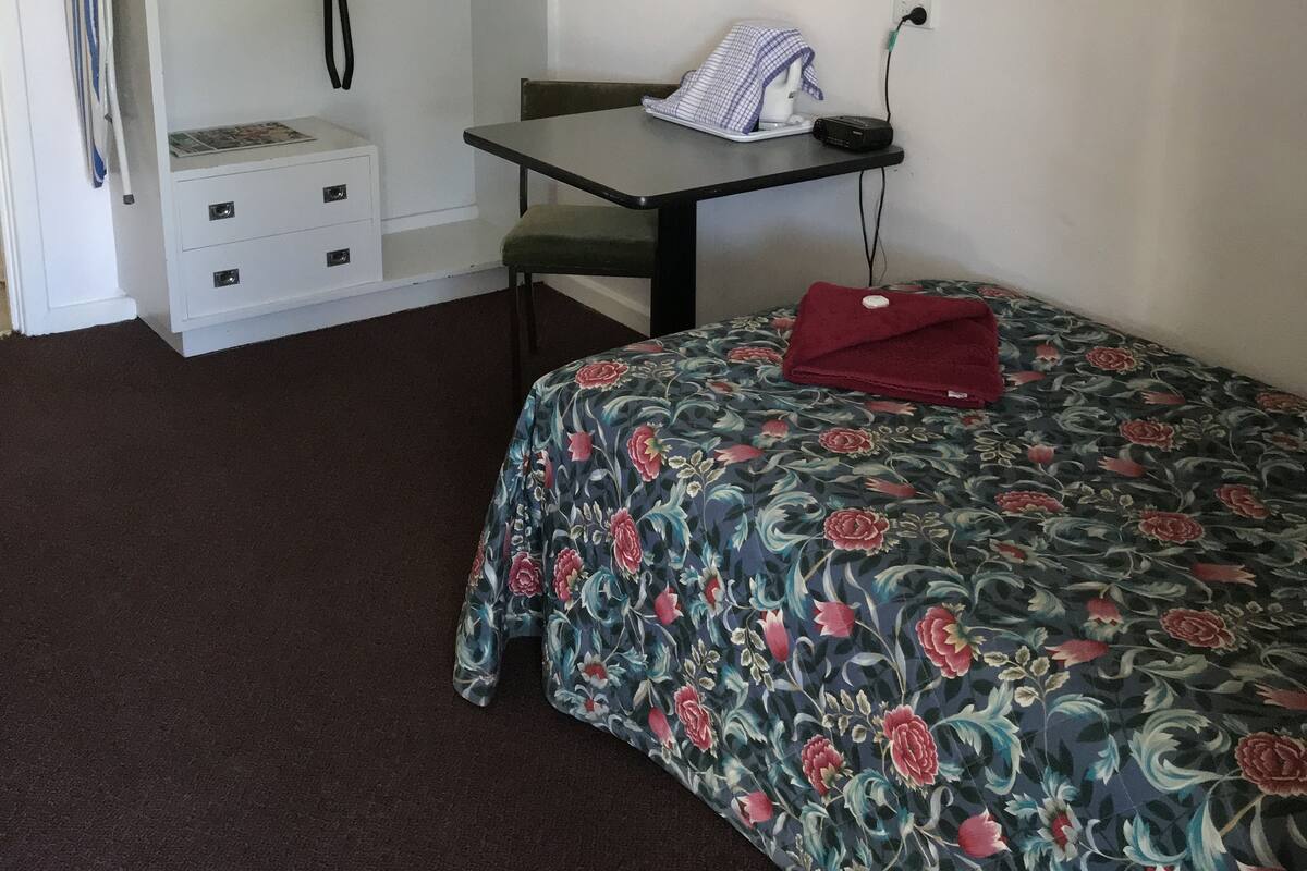A compact room with a bed, a desk with a chair, a wardrobe, and a mirror.