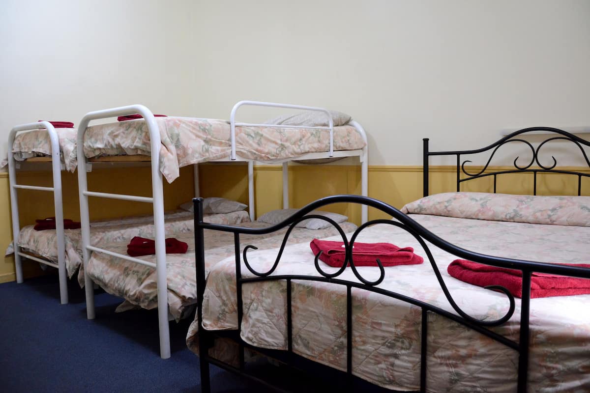 A room with bunk beds and a single bed, both with floral bedding and red towels.
