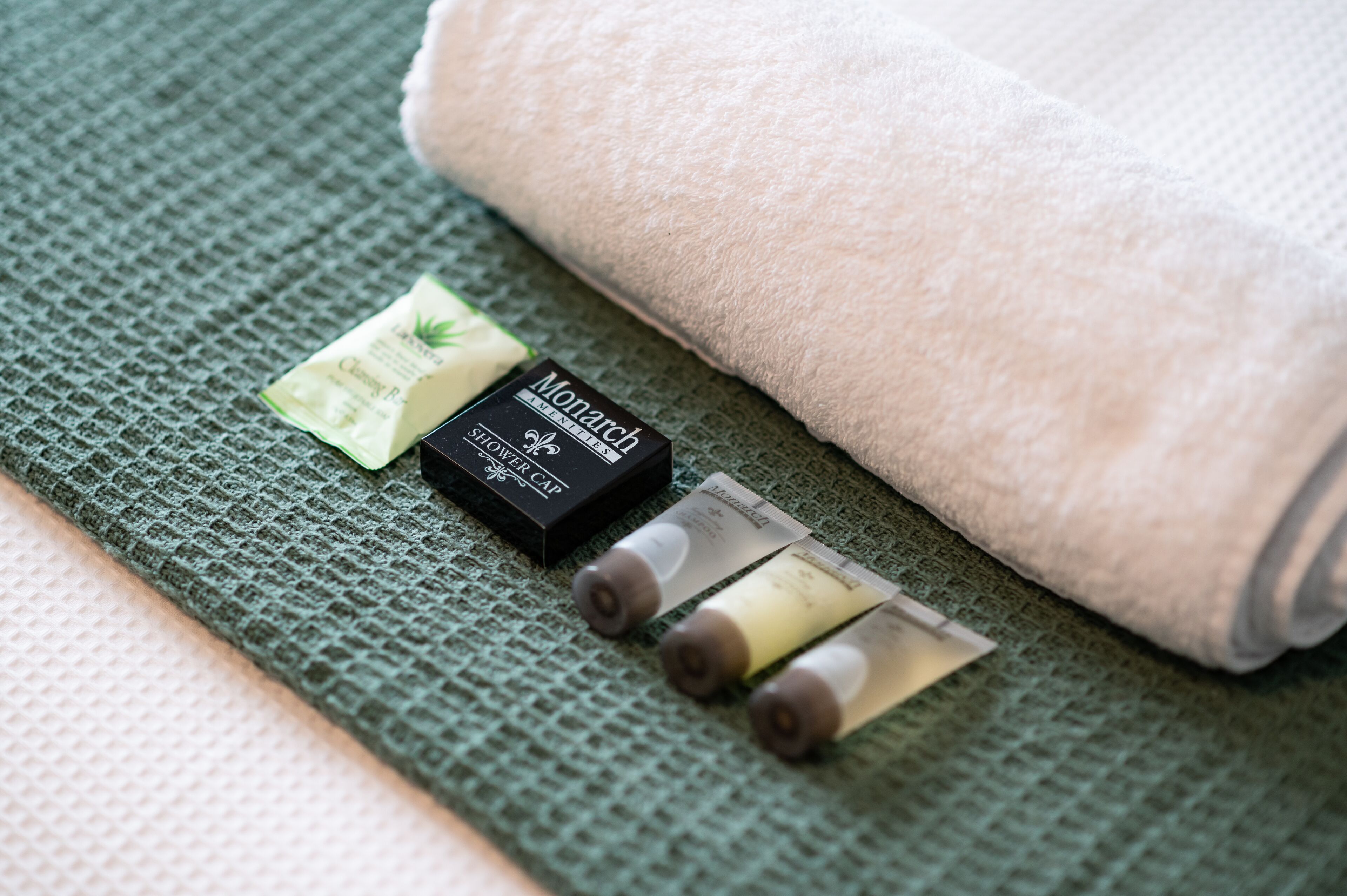 A green textured surface with a beige towel, a Monarch brand hair cap, and a small packet of shampoo.