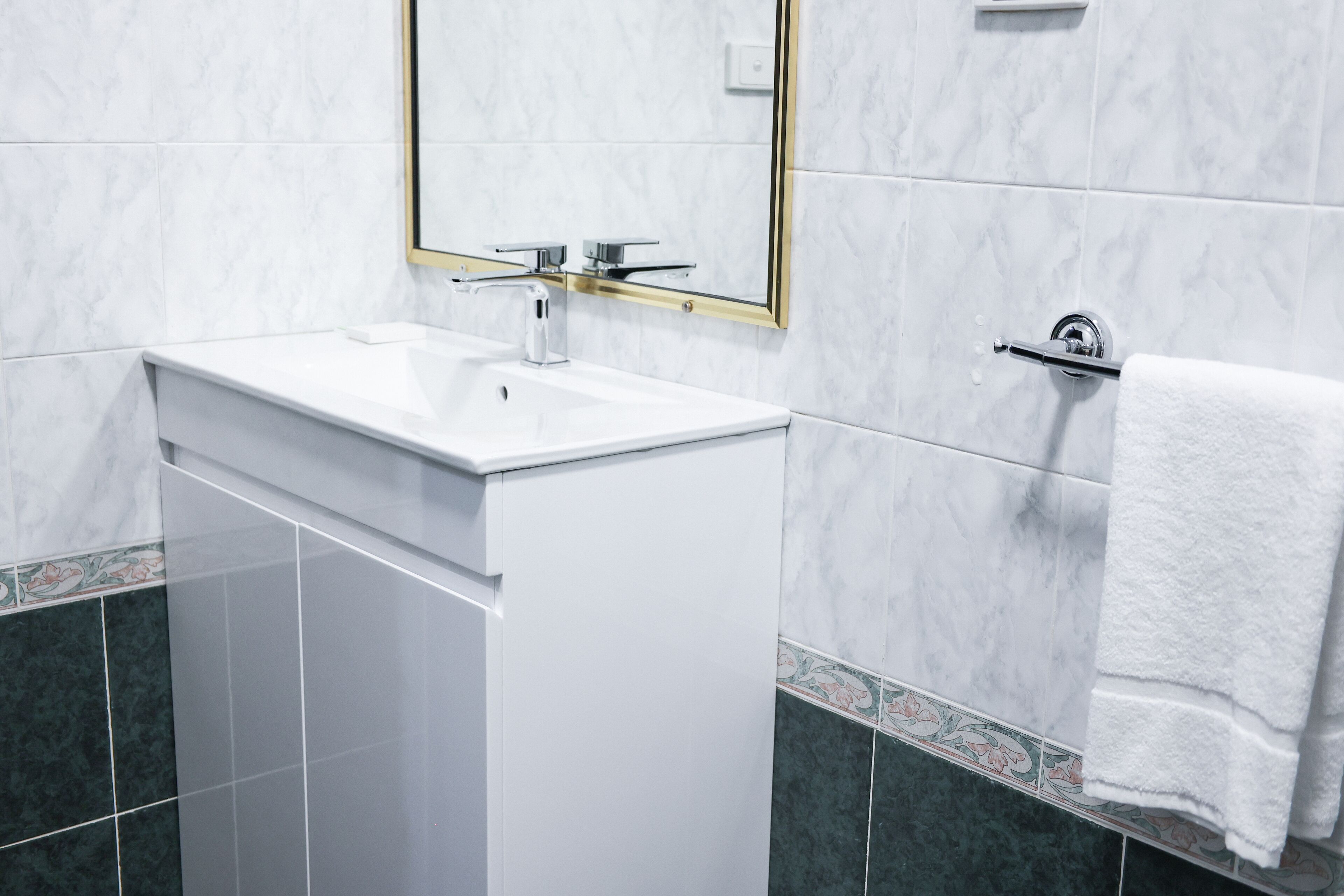 A bathroom with a white sink, a mirror with a gold frame, and a towel rack.