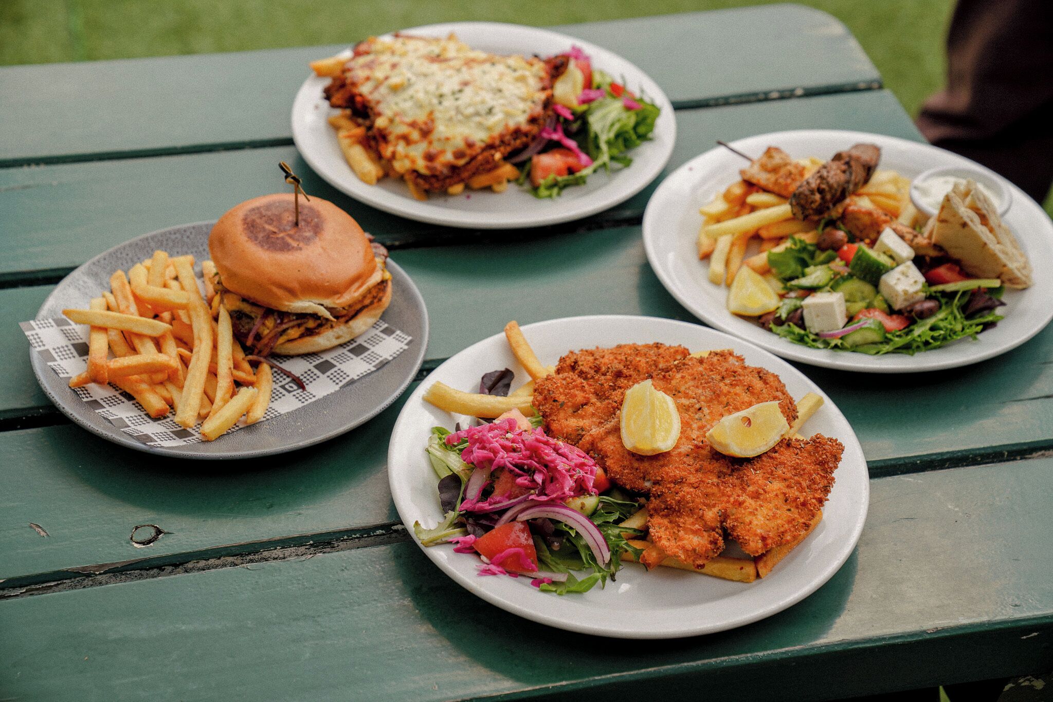 Et bord med fire tallerkener mad, herunder en burger, pommes frites og en salat.