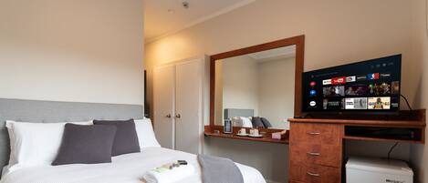 Habitación de hotel con cama, escritorio con computadora, refrigerador pequeño y televisor que muestra servicios de transmisión.