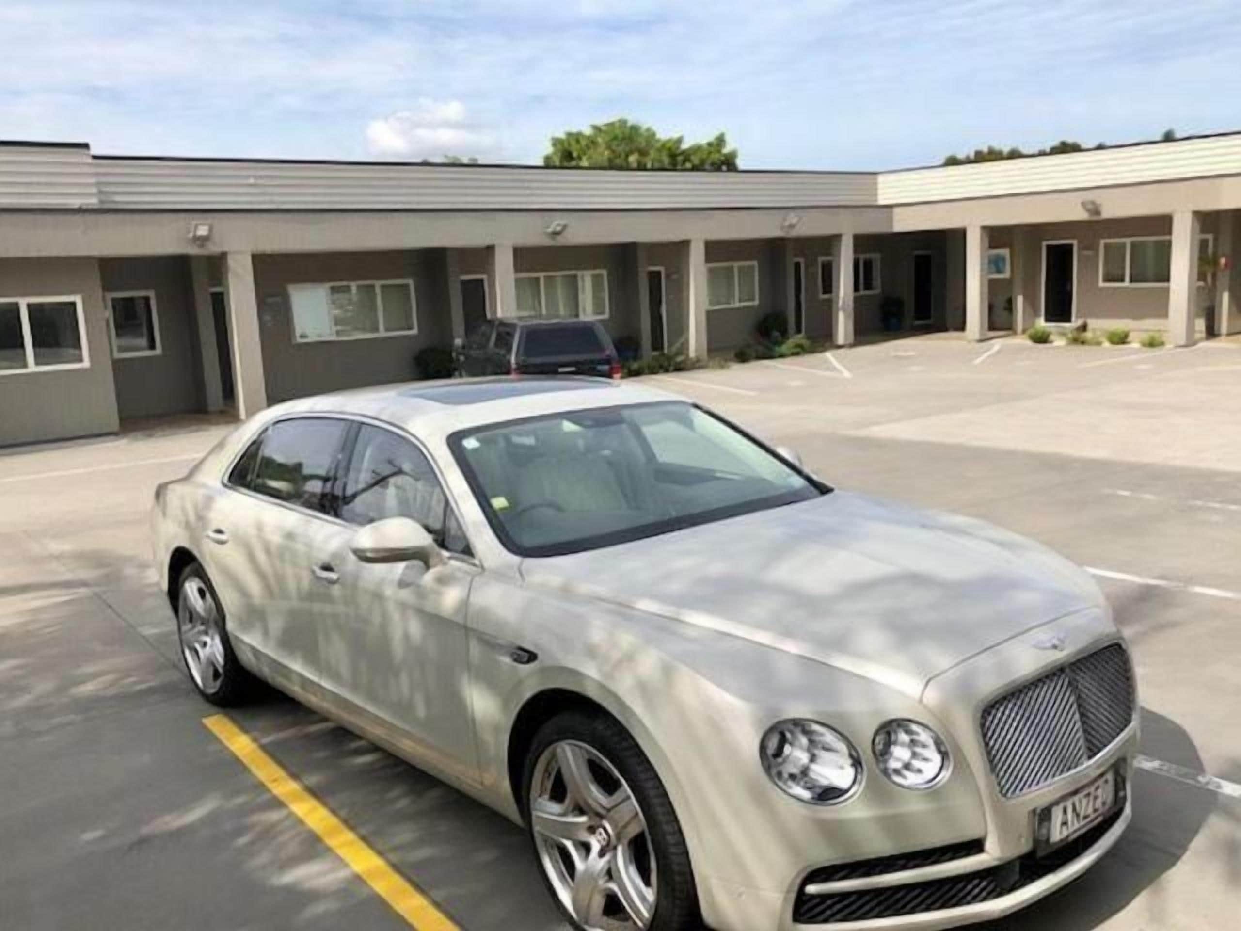 A silver Bentley parked in a parking lot with a building in the background.
